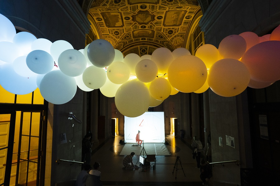 Performer in the Between Air & Waterlines event. The performer is kneeling on stage with balloons in the foreground