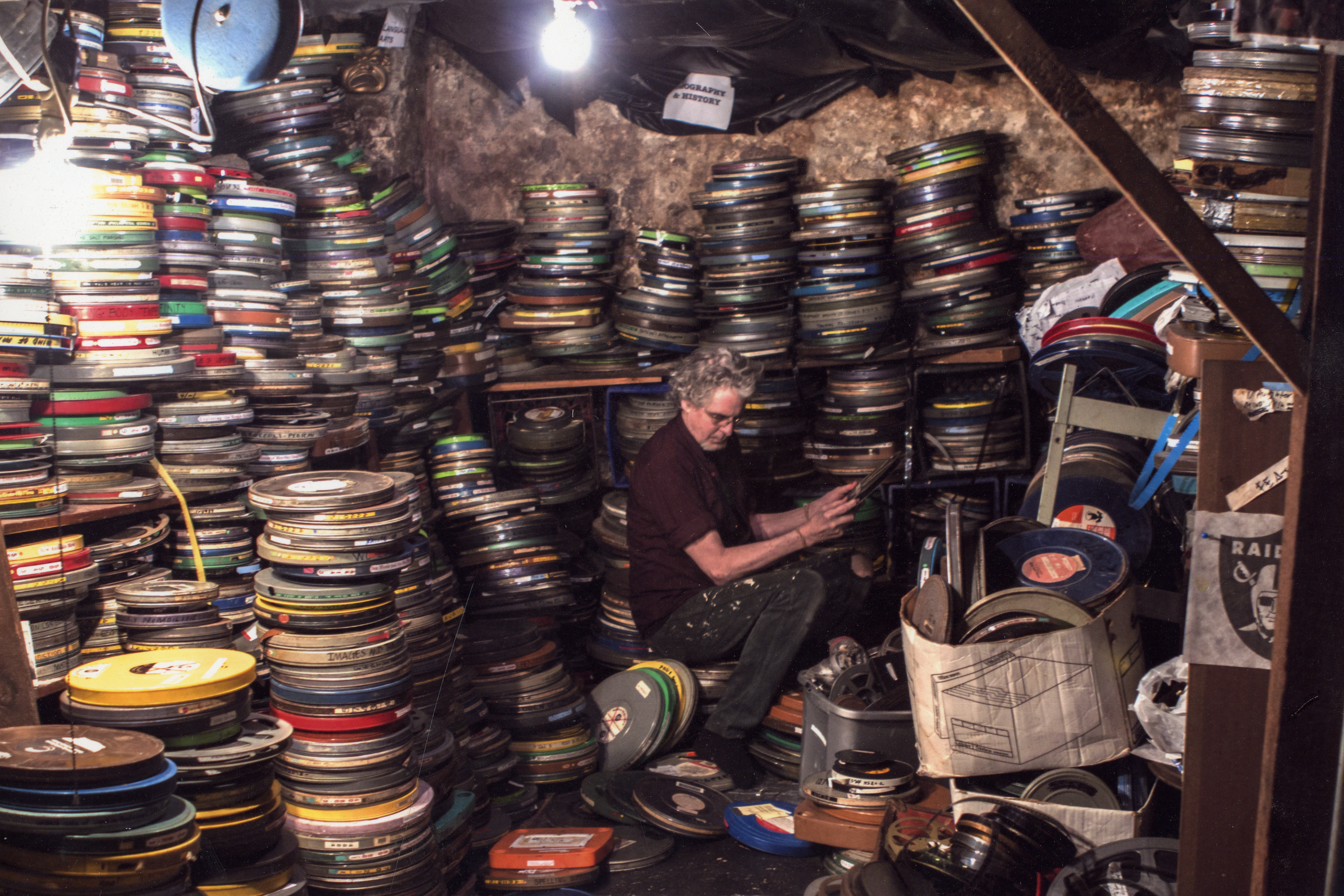 Filmmaker Craig Baldwin surrounded by cans of film reels