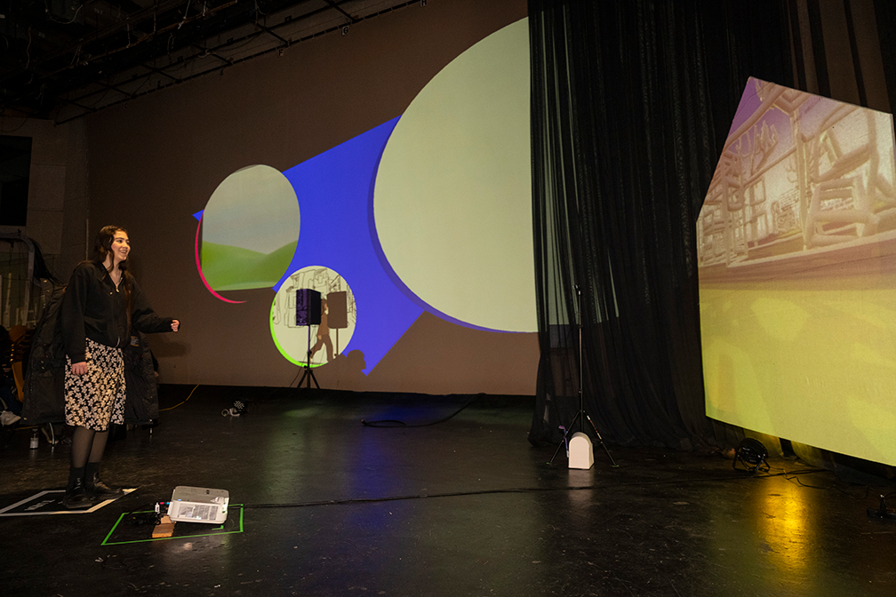 a student stands on a square marked on the floor, interacting with an animation projected into a house-shaped screen
