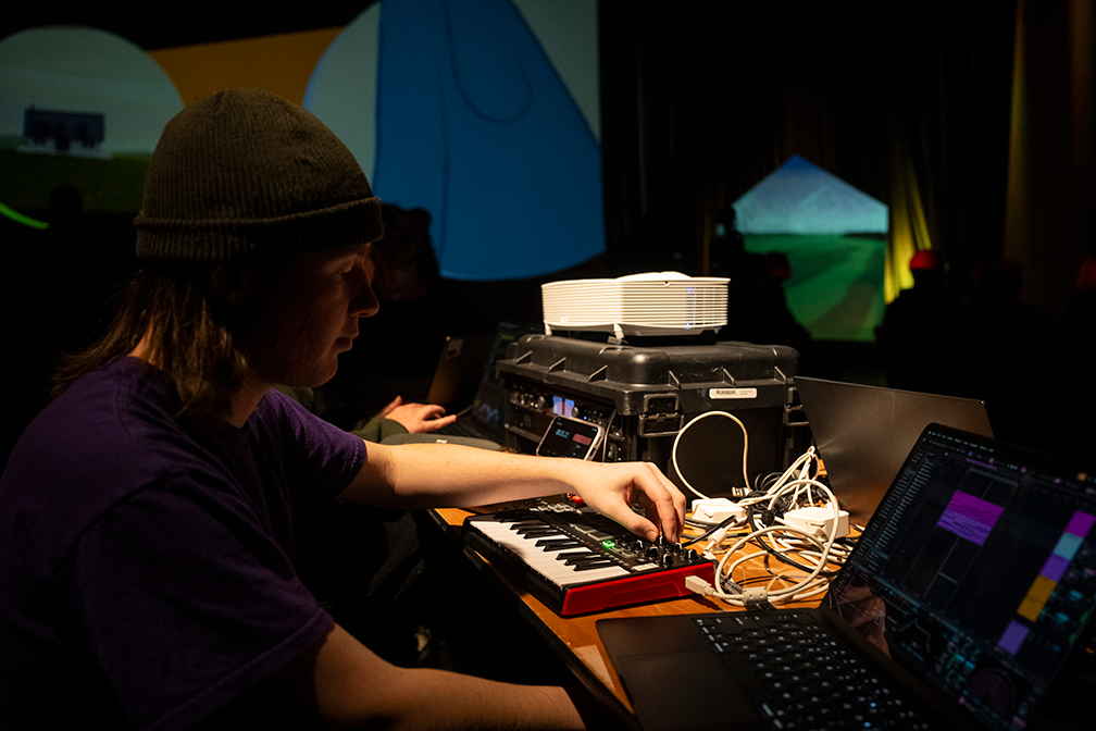 a student in a purple t shirt and black hat adjusts dials on a keyboard