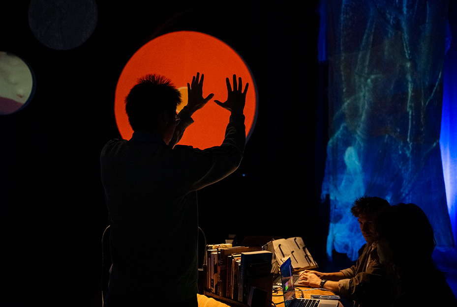 an attendee with two hands outstretched is silhouetted before a glowing orange circle
