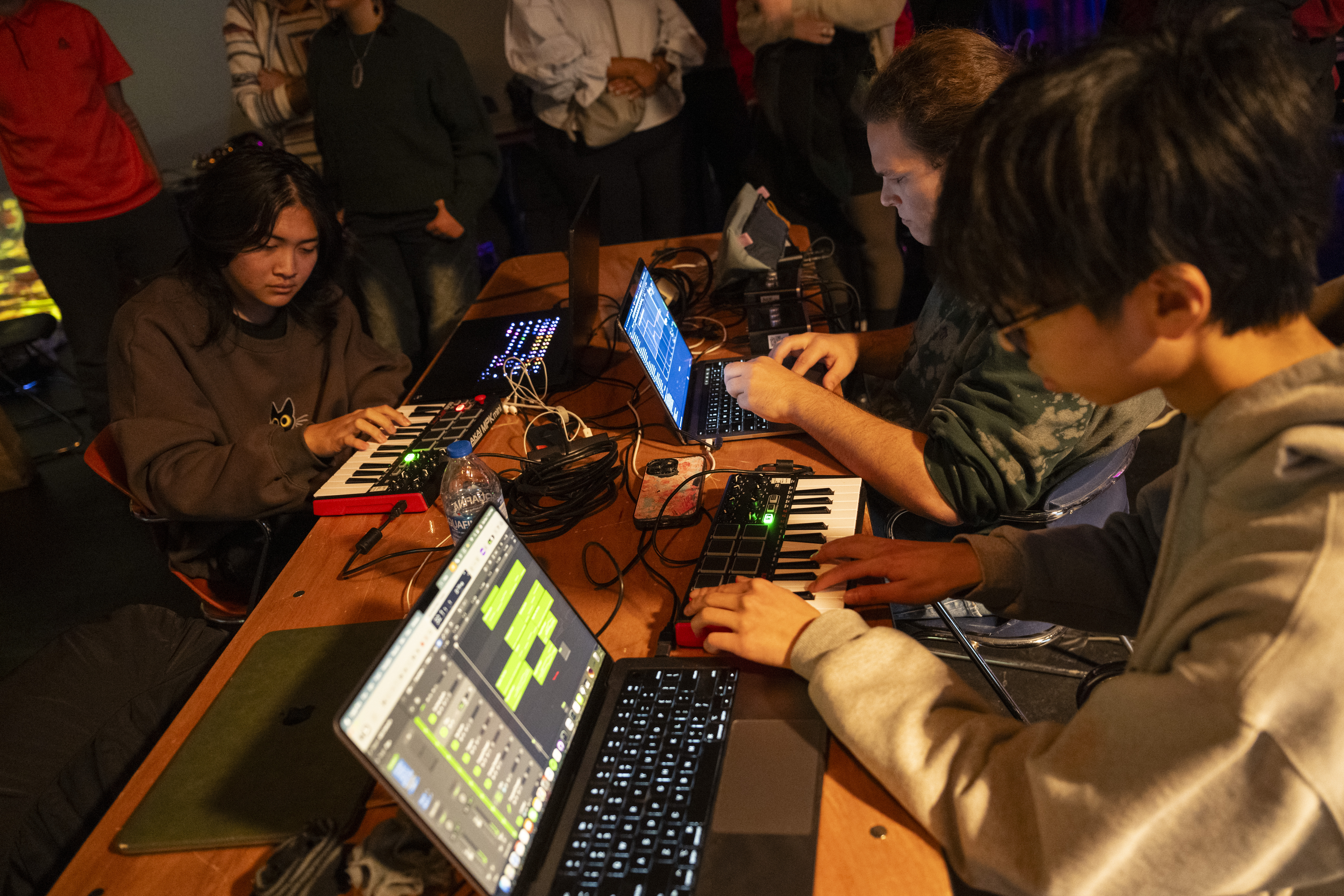 three electronic musician work from laptops and synthesizers during a performance