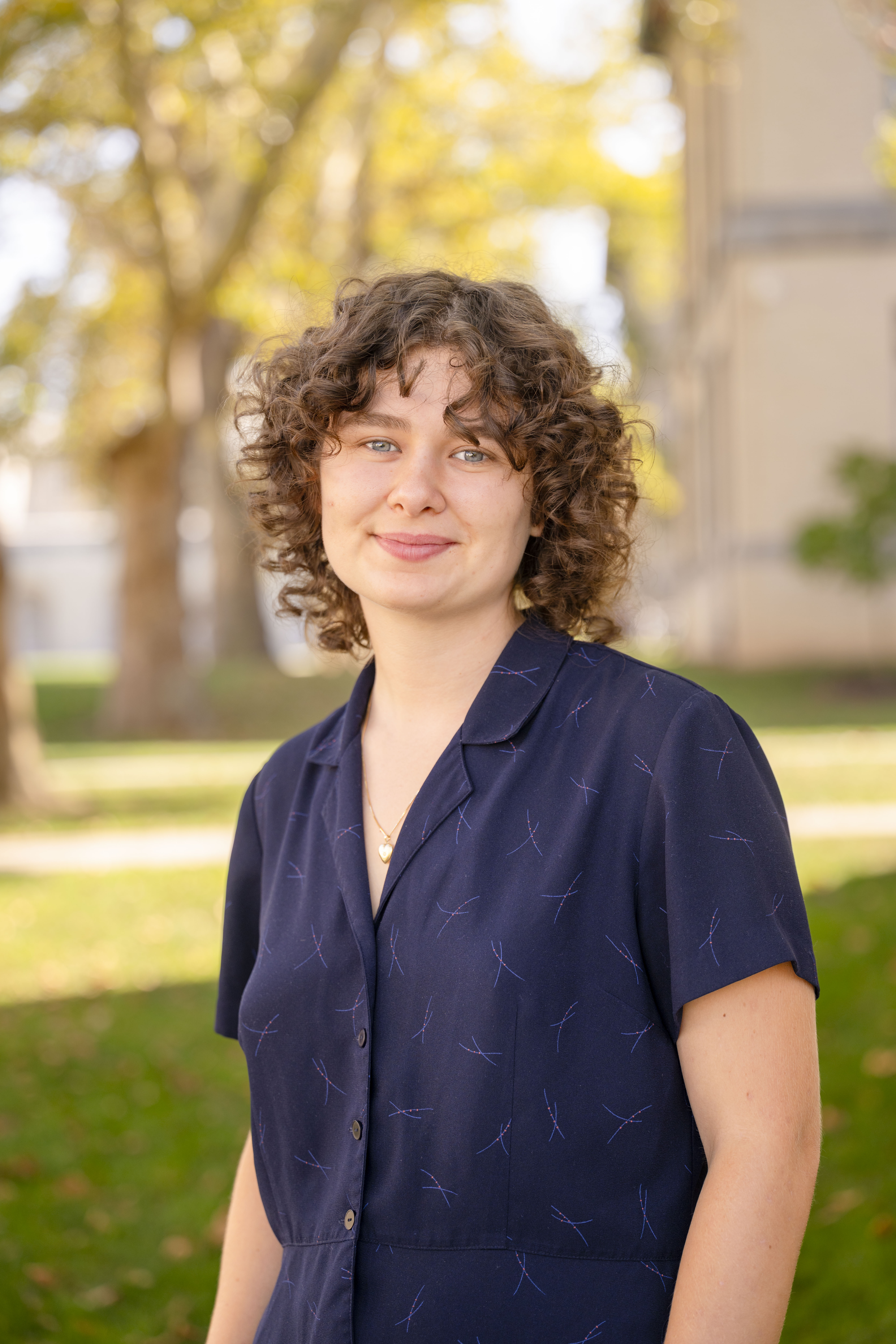 a portrait from the waist up of Kat, with short curly hair and a dark blue collared shirt