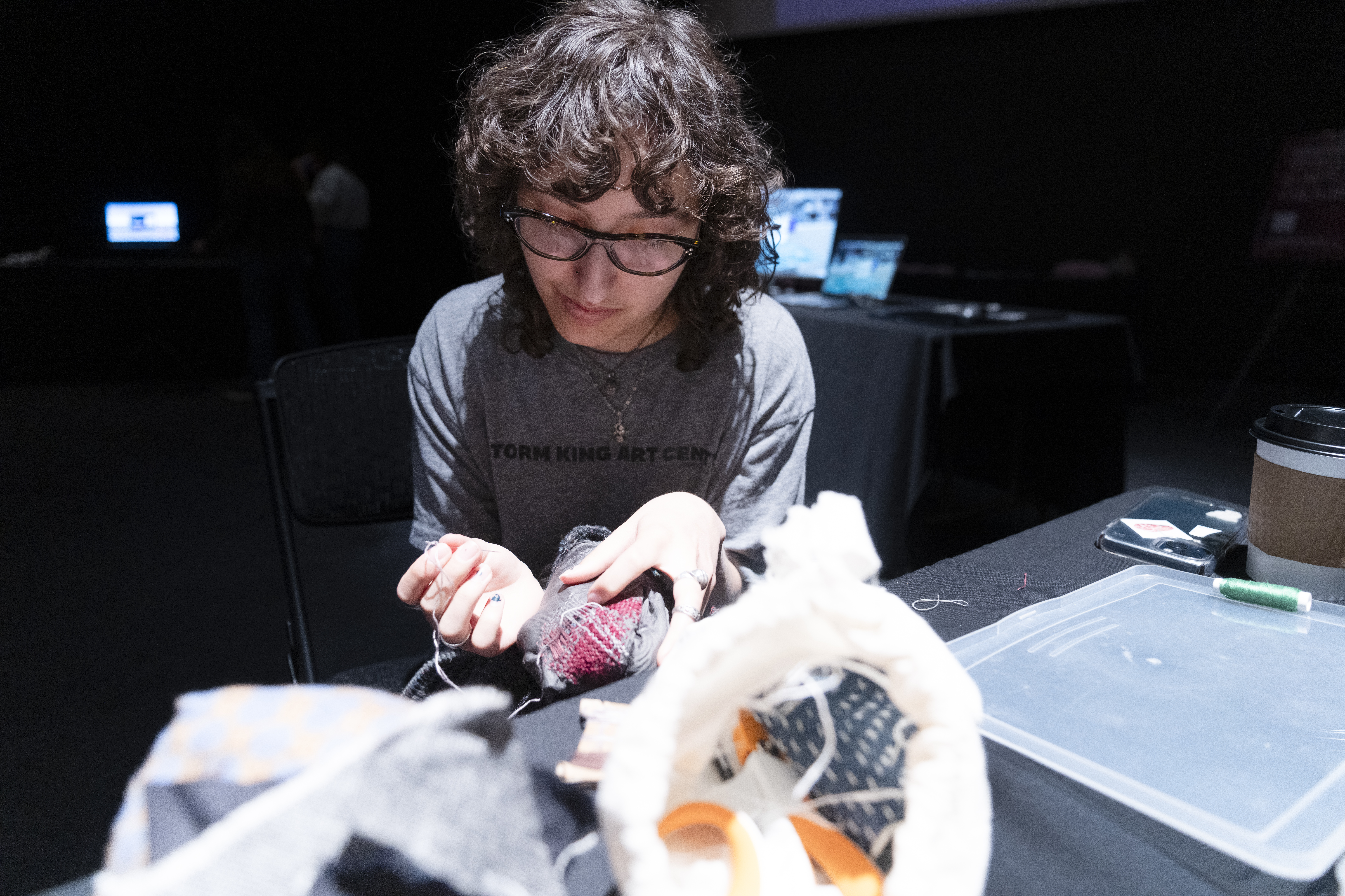 a student with dark curly hair and glasses mends a torn piece of clothing