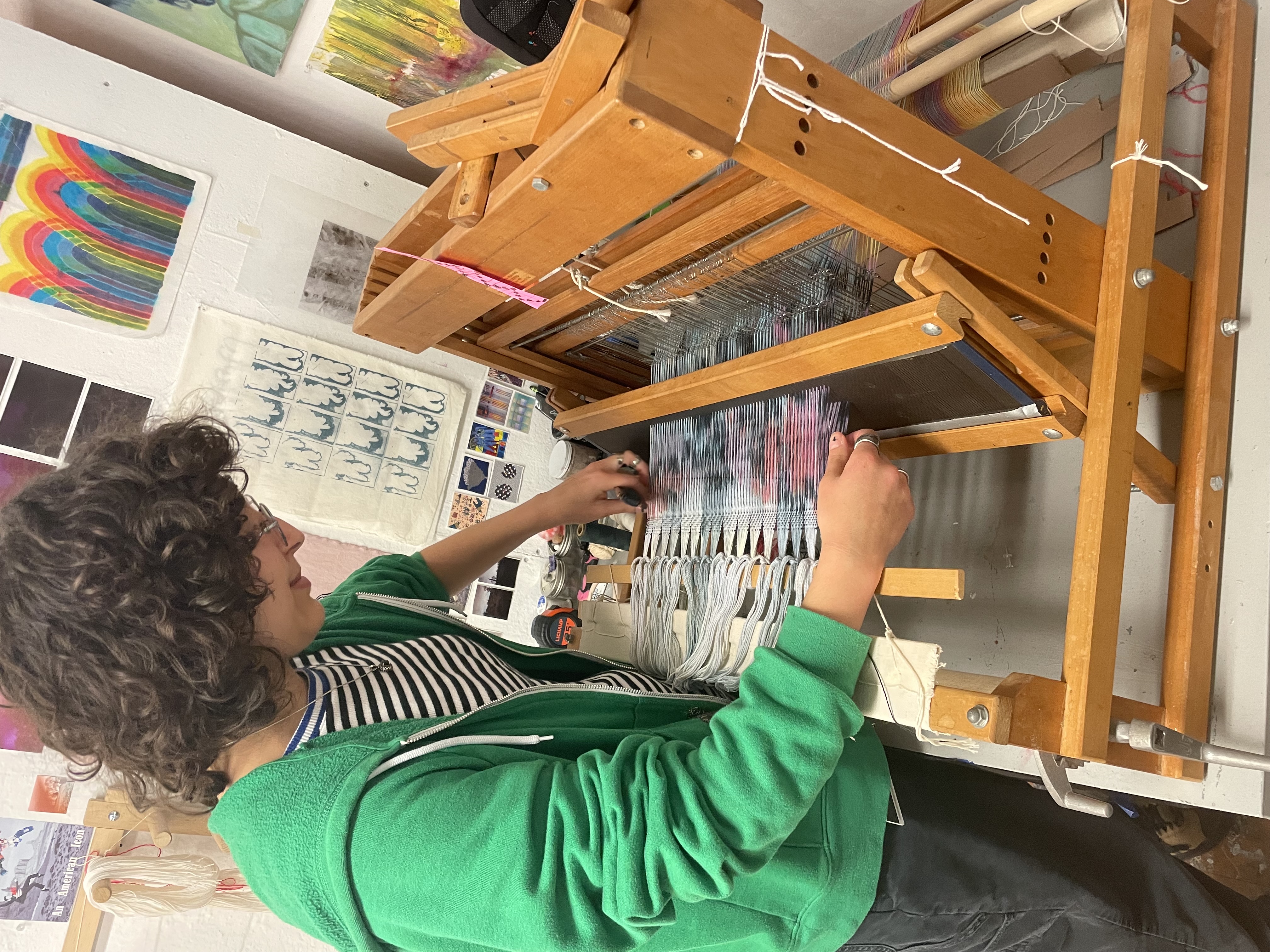 a student works with a multicolored woven fabric on a wooden tabletop loom