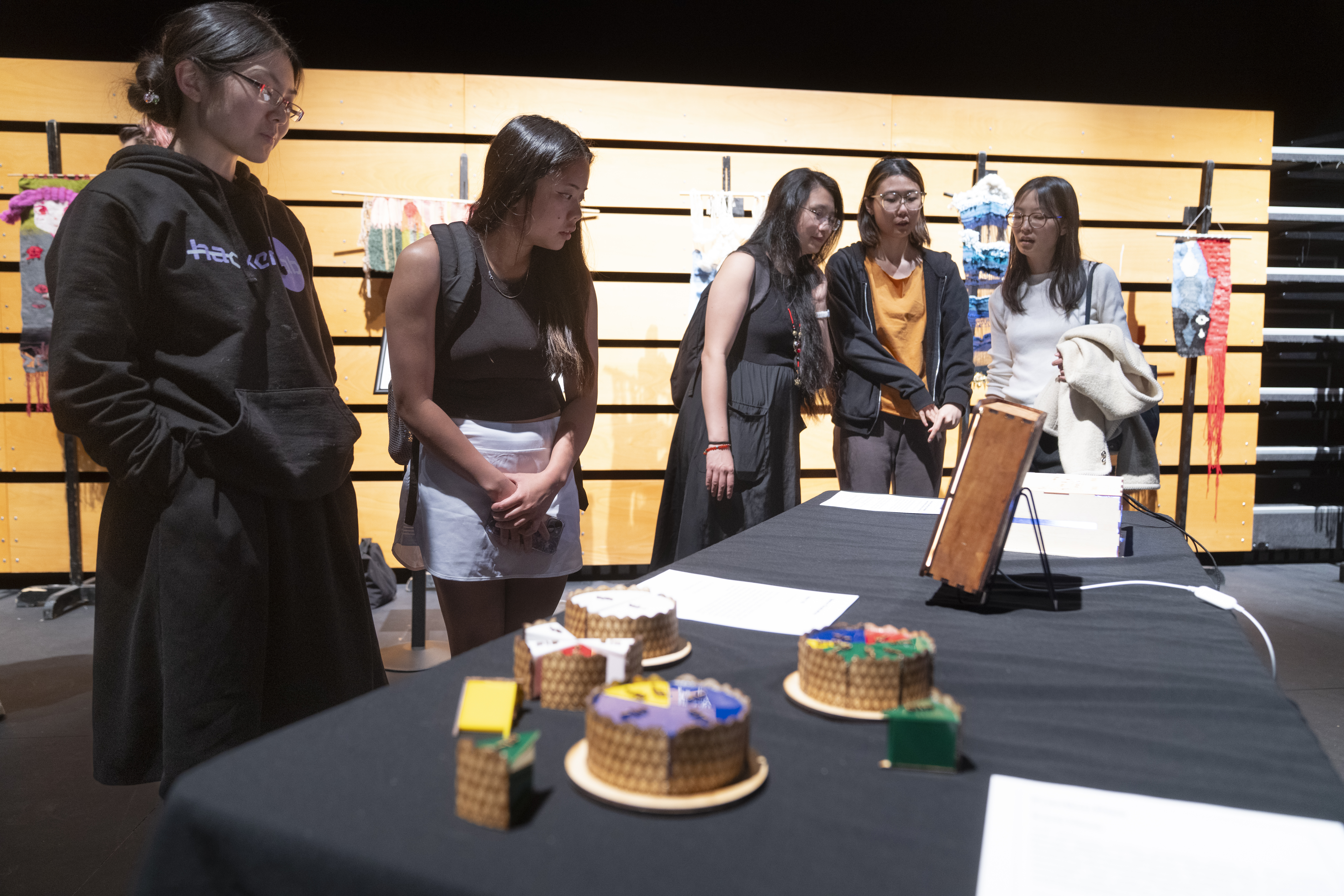 five attendees stand around a table with a black tablecloth that holds thee complete fraction pies made up of different fractions, and several additional pieces of different sizes
