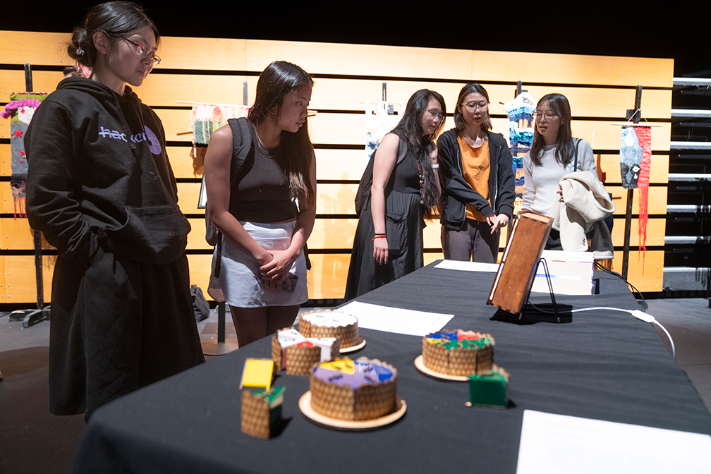 five attendees stand around a table with a black tablecloth that holds thee complete fraction pies made up of different fractions, and several additional pieces of different sizes
