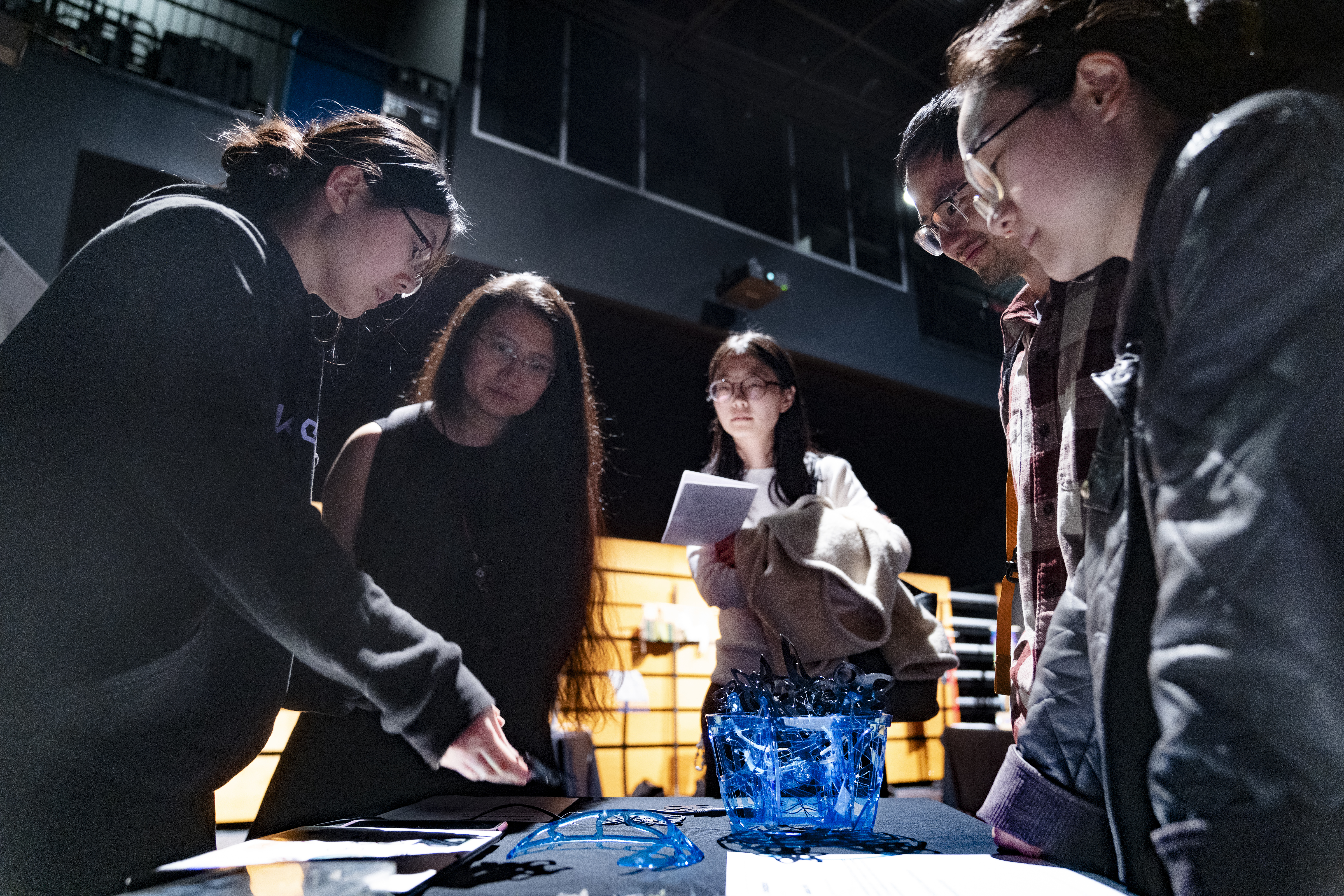 five attendees look down at a table with a blue structure
