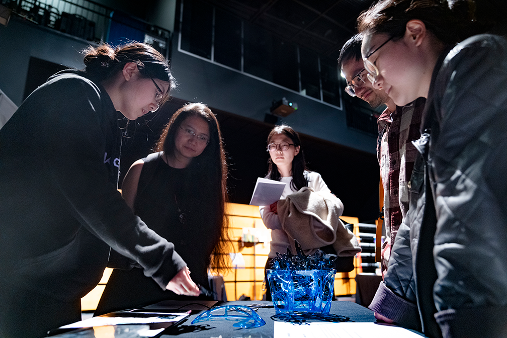 five attendees look down at a table with a blue structure