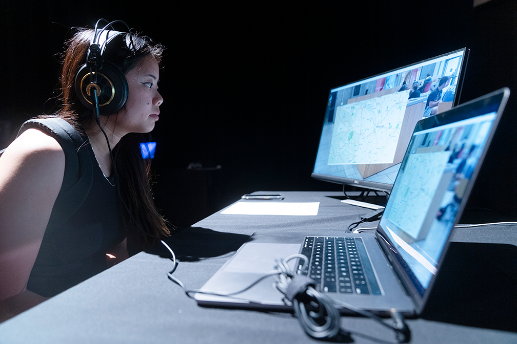 a student wearing headphones looks at a video on two computer screens