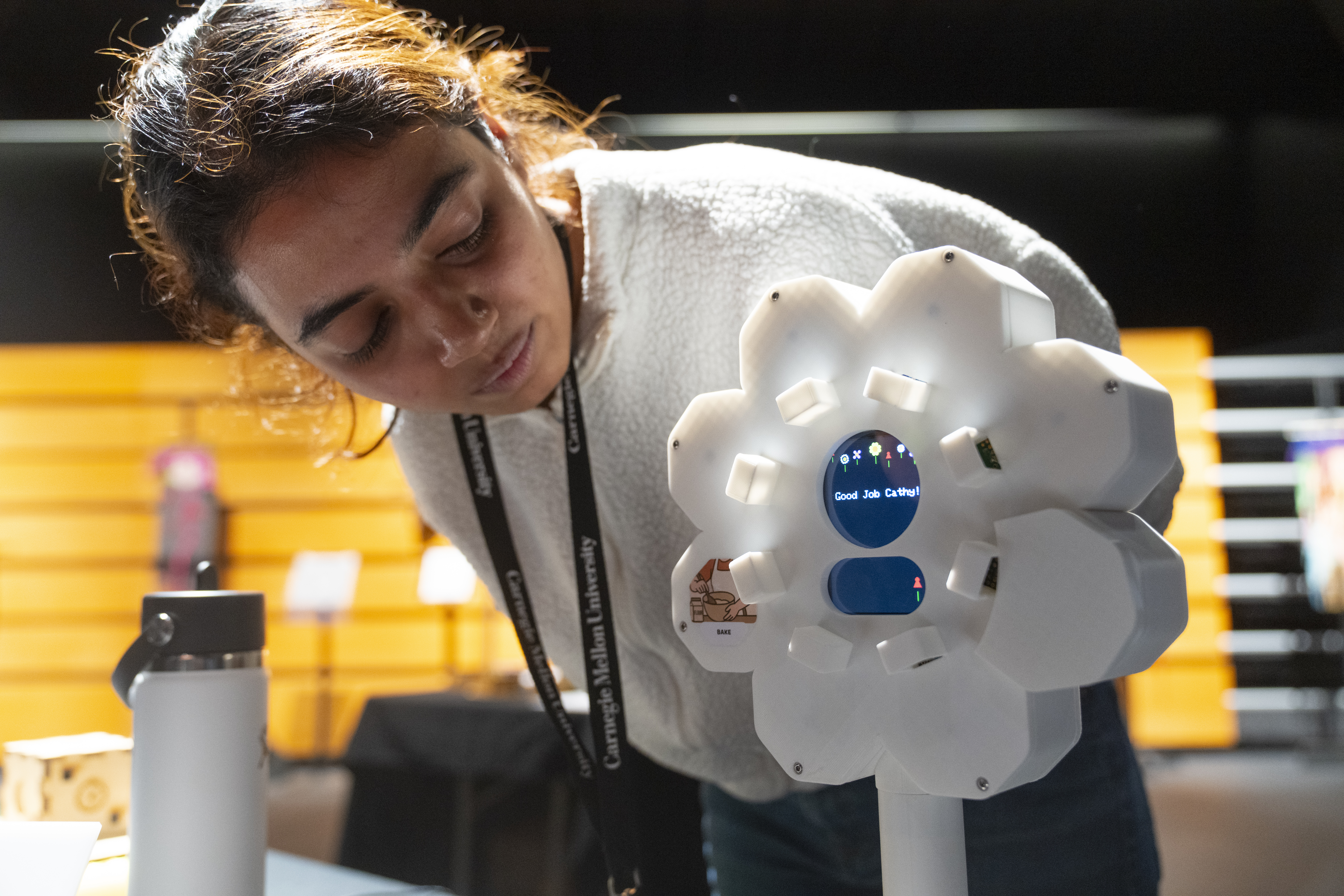 a student inspects a white flower-shaped device reading "Good Job Cathy!"