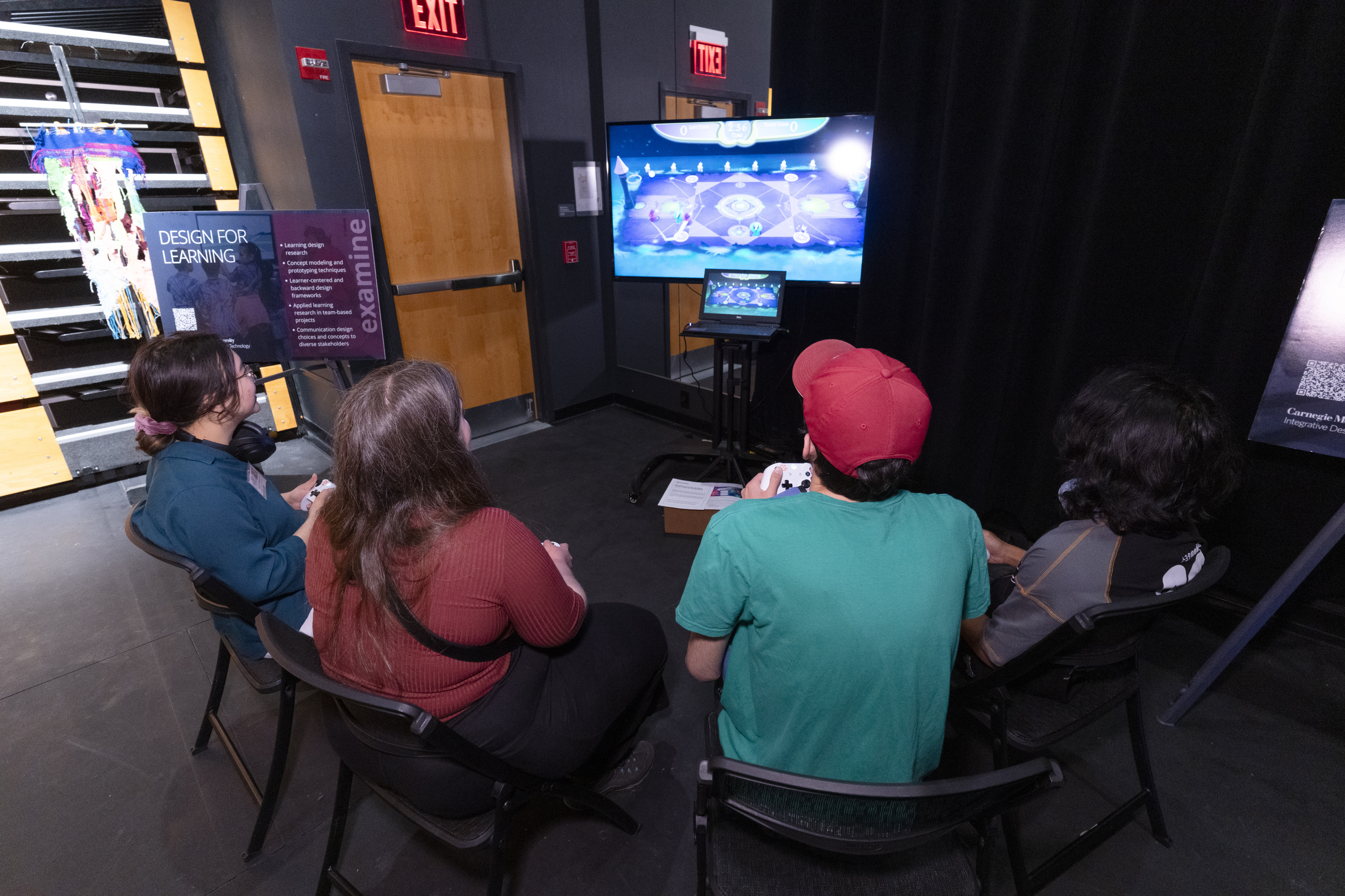 four people holding controllers gather around a large screen