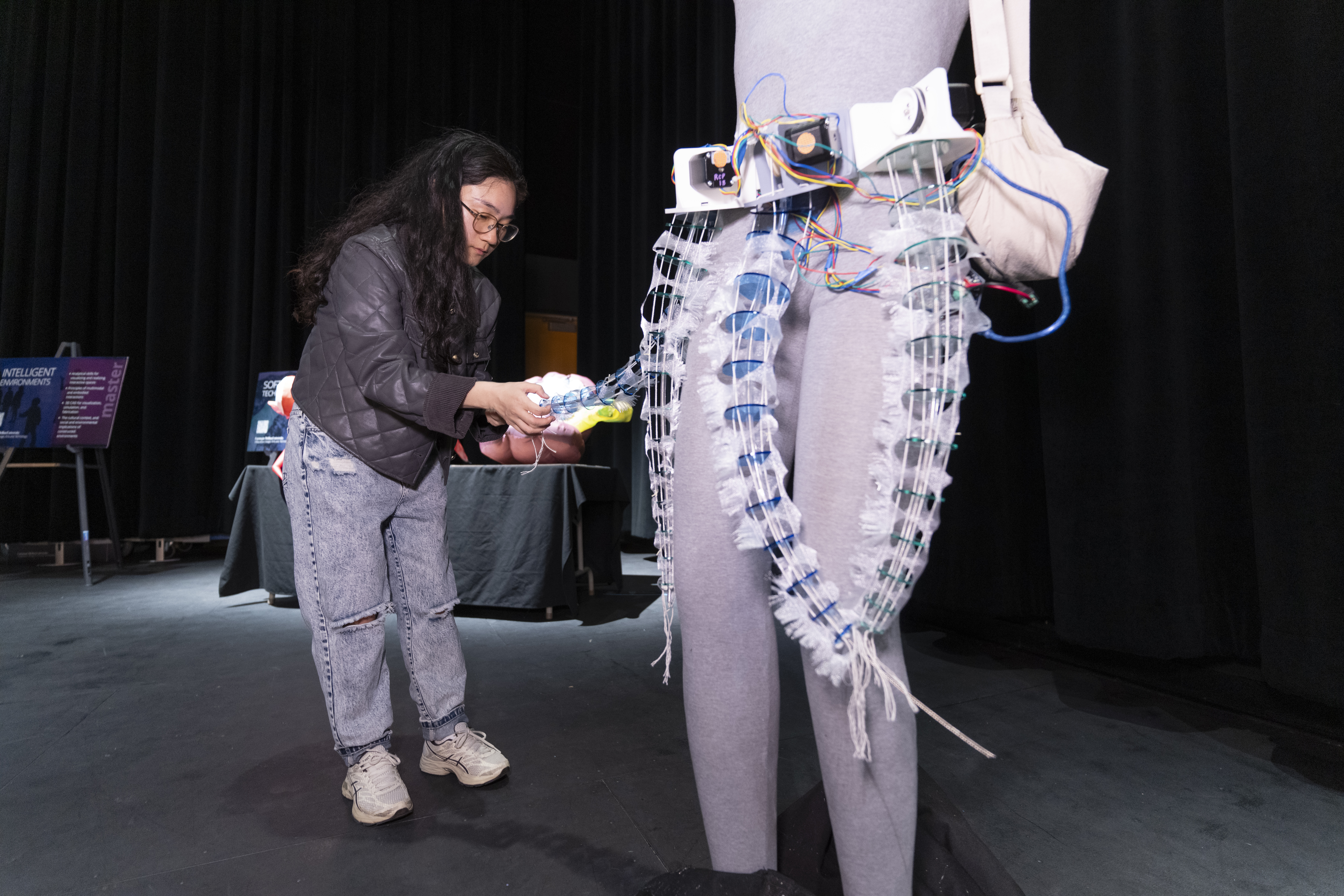 a student in jeans and a jacket holding a tentacle attached to a belt on a mannequin