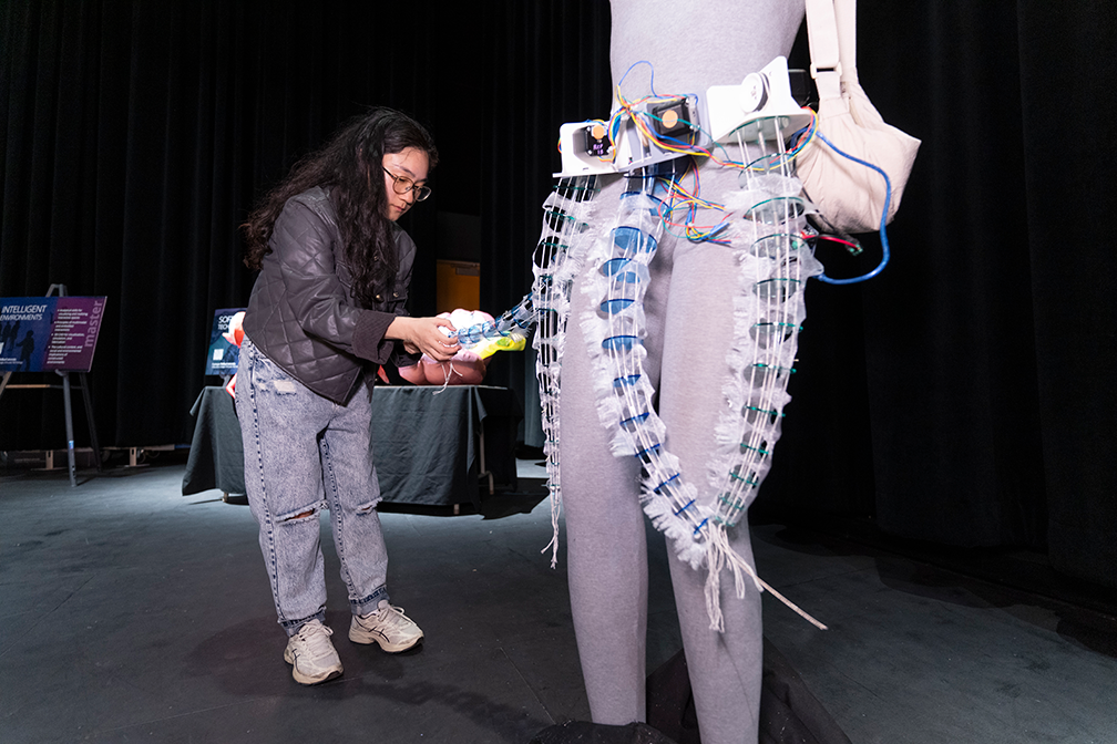 a student in jeans and a jacket holding a tentacle attached to a belt on a mannequin