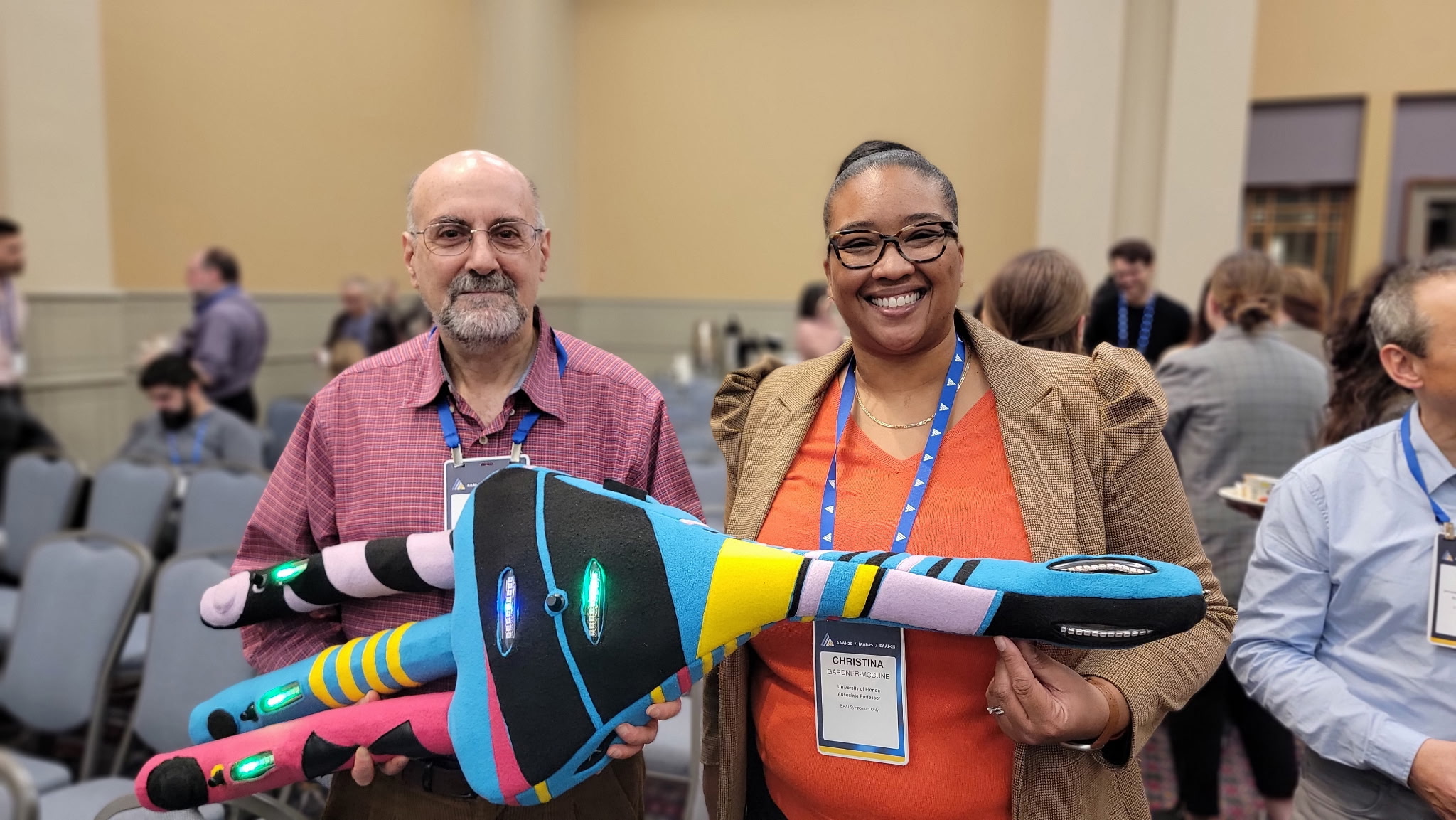 Touretzsky and McCune pose with a 3-legged, multi-colored, glowing neuron in a conference room with chairs in the background
