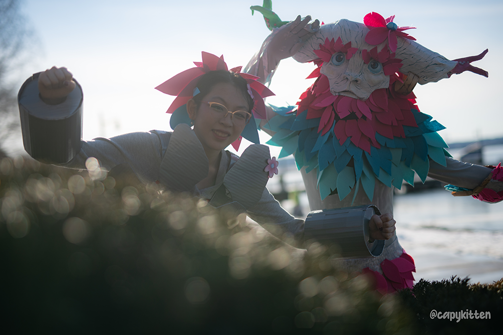 two cosplayers dressed in bright pink and teal, one with a petal headpiece and one with a mask