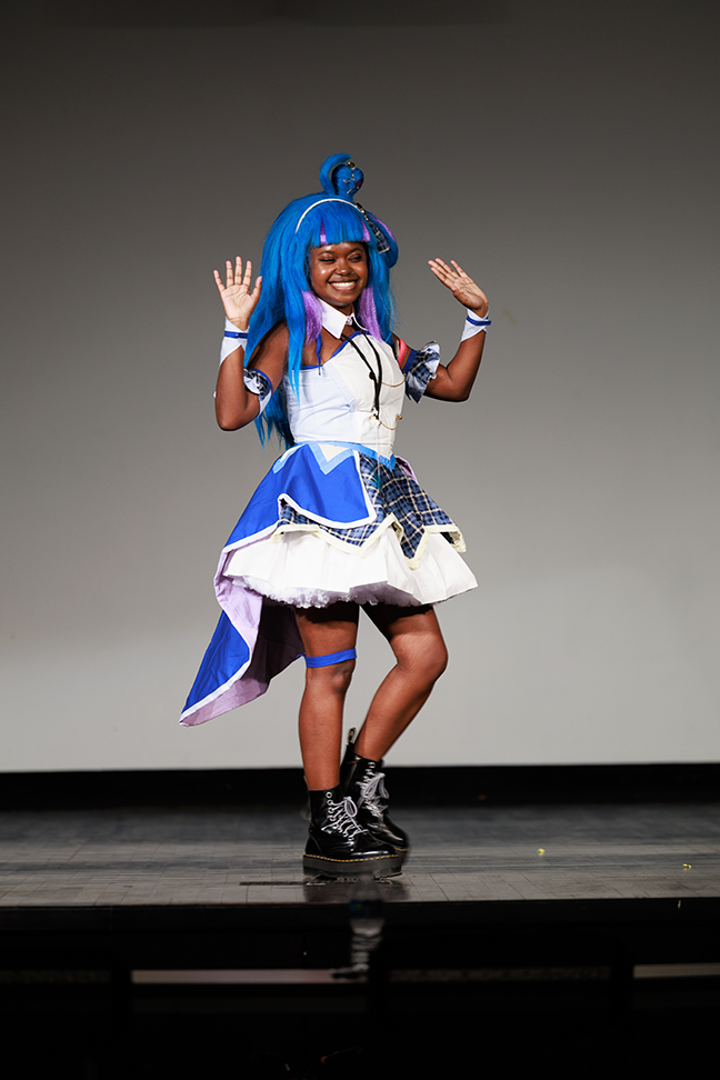 a Black cosplay artist in a bright blue wig, with a blue and white outfit and black combat boots